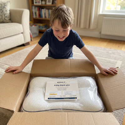 A boy opening the Hushly Kids box on the living room floor, the pillow inside.