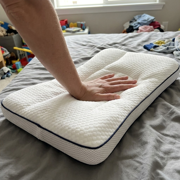A hand pressing the Hushly Kids pillow, showing the knit cover and the navy piping.
