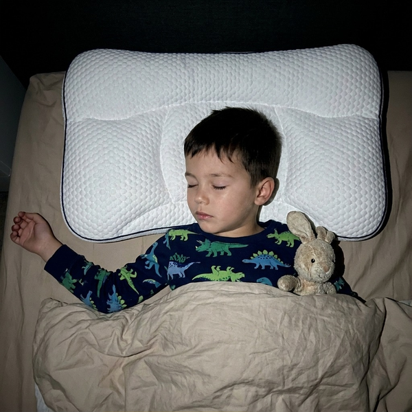 Boy asleep on his back on the Hushly Kids pillow, holding a soft toy
