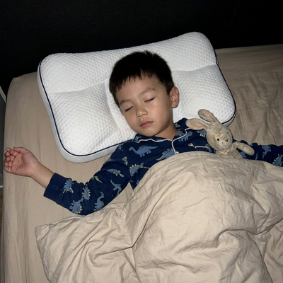 A boy asleep on his back on the Hushly Kids pillow, arms stretched out.