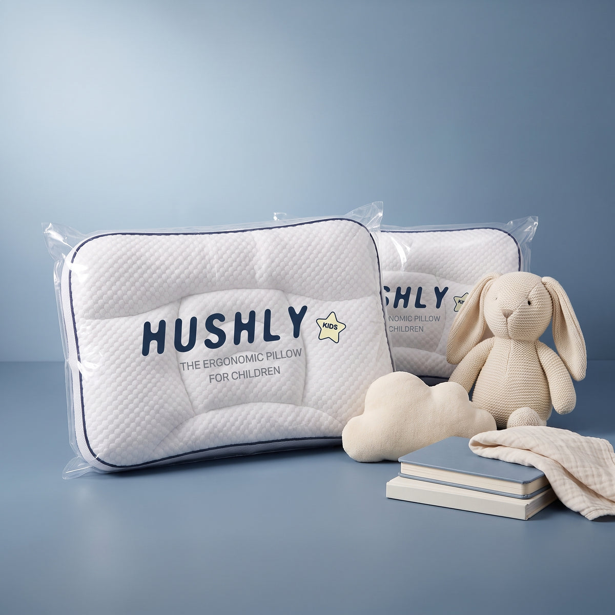 Two Hushly Kids pillows in their packaging beside a knitted bunny and a cloud cushion